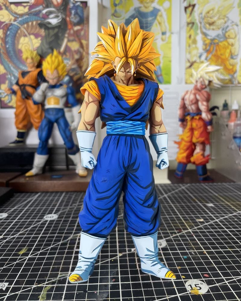 A Dragon Ball Z Super Saiyan Gohan action figure standing on a gridded cutting mat, with other Dragon Ball figures blurred in the background.
