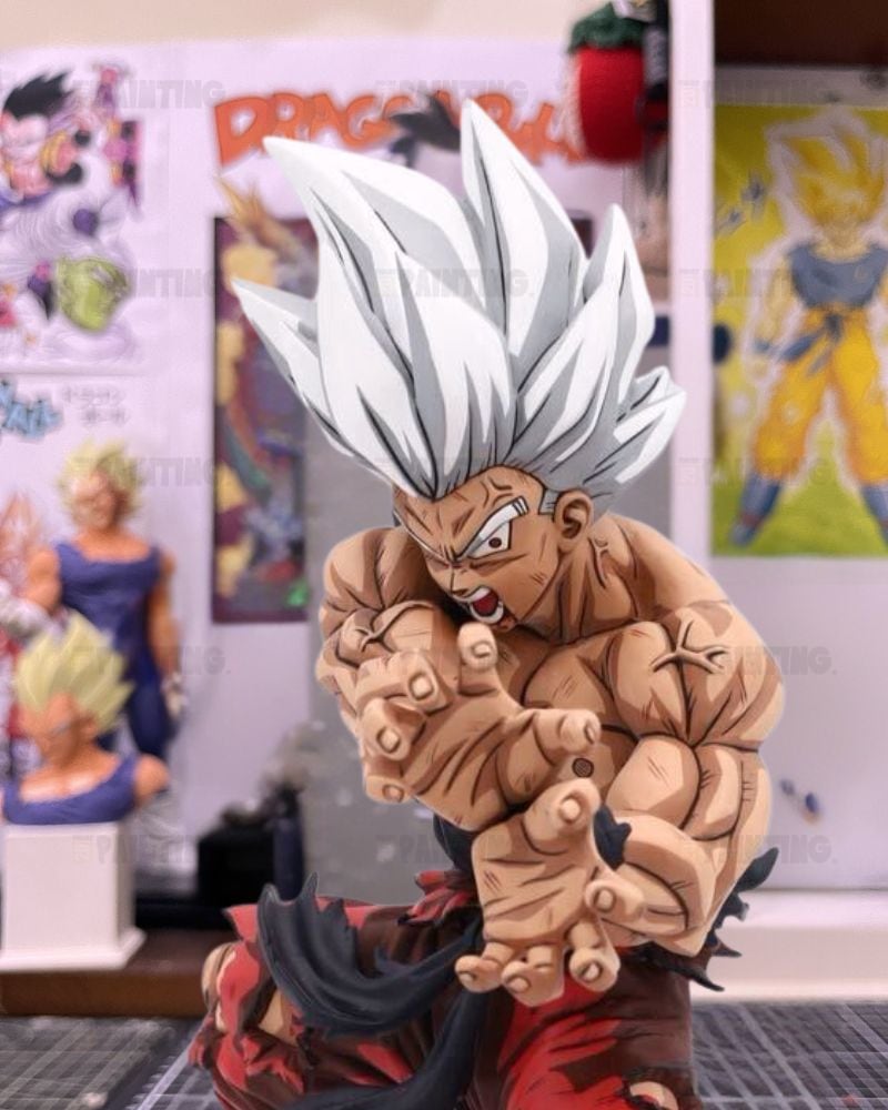 A detailed collectible figurine of a Super Saiyan character from Dragon Ball, posed in a dynamic fighting stance with white spiky hair, tan skin, and a red and black outfit, set against a blurred background of anime posters and other figurines.