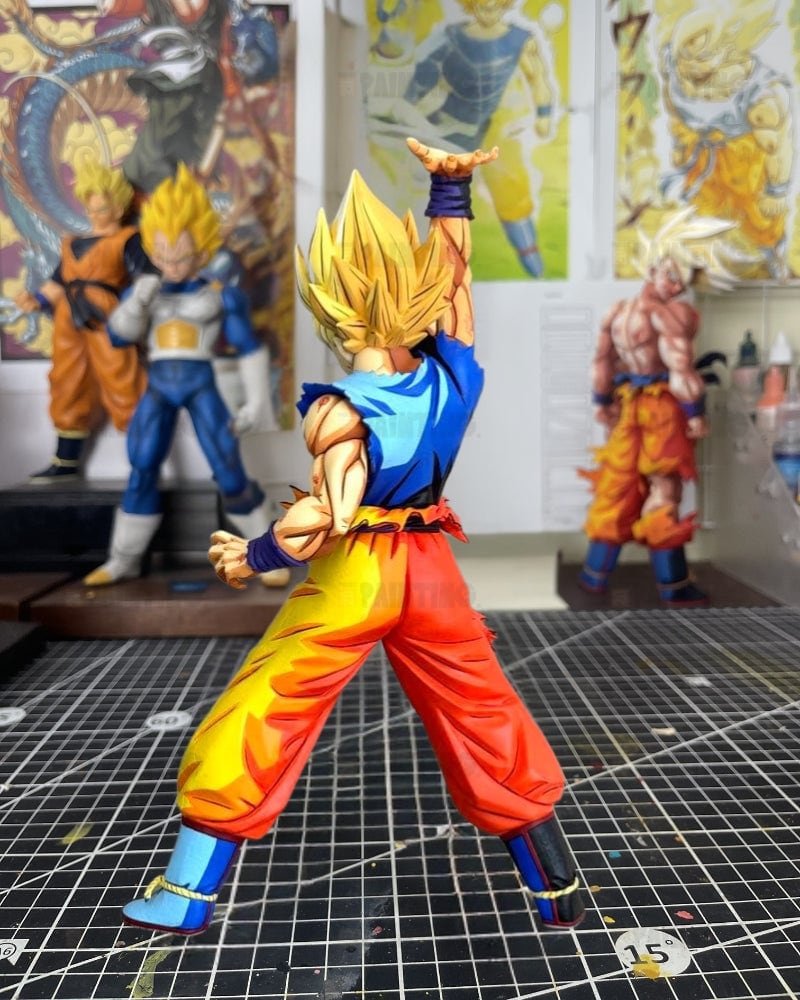 A Super Saiyan Gohan action figure from Dragon Ball Z, shown from the back in a dynamic pose on a cutting mat with other anime figures in the background.