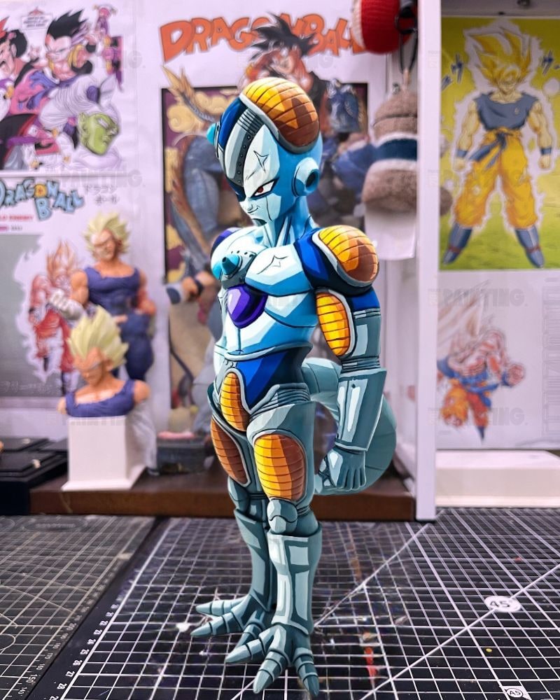 A custom-painted Dragon Ball figure of Frieza with blue, white, and orange armor, standing on a black gridded cutting mat in a collector's room with Dragon Ball posters in the background.