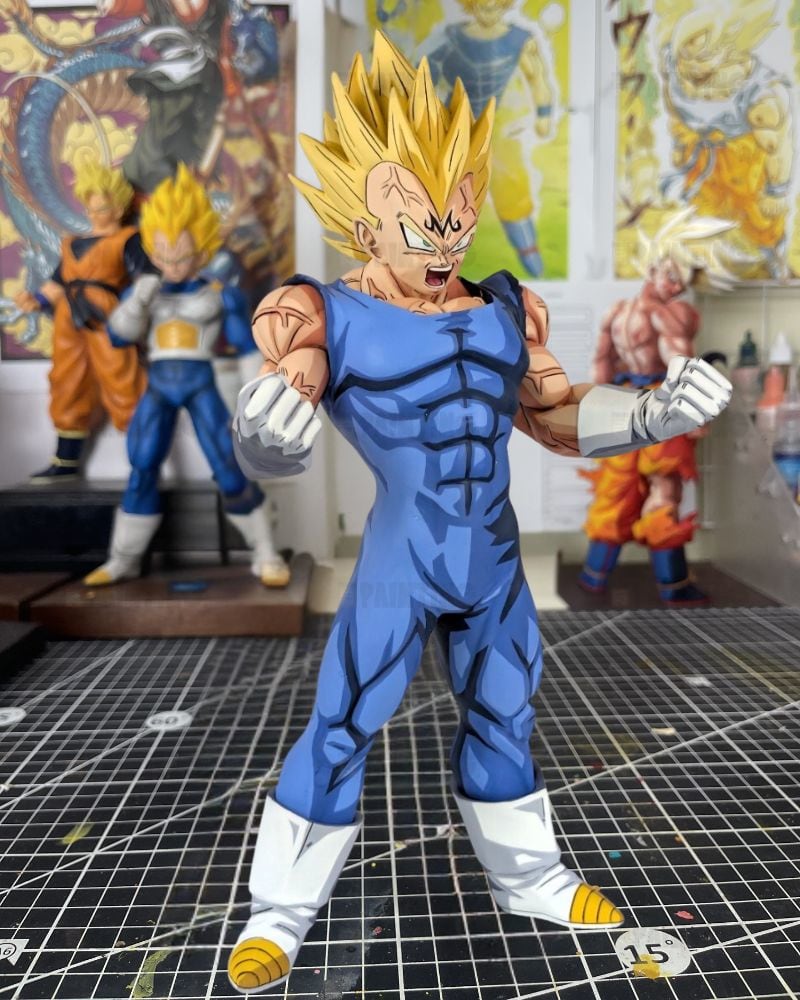A detailed collectible action figure of Vegetto from Dragon Ball Z, standing on a gridded cutting mat in a collector's room with other anime figures in the background.