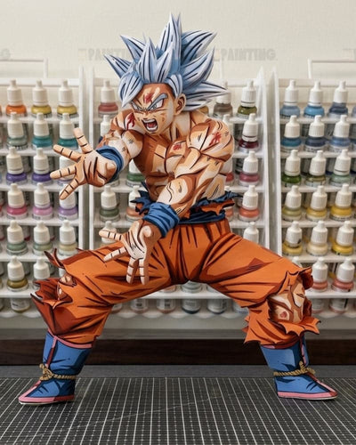 A detailed anime figure of Goku in a Super Saiyan pose, featuring spiky blue hair, torn orange gi pants, and blue boots, posed in front of shelves of paint bottles.