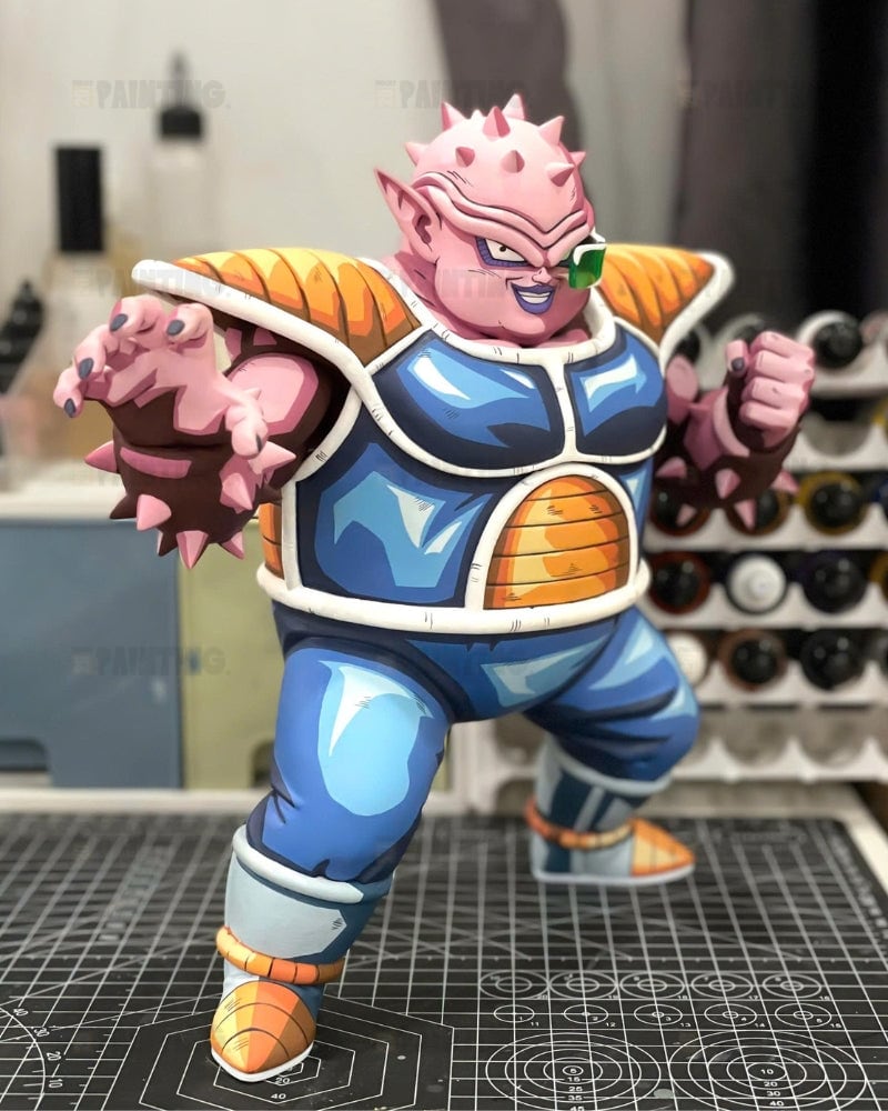A detailed collectible figurine of a pink-skinned anime character in a blue and orange battle armor pose, standing on a gridded cutting mat in a workshop setting.