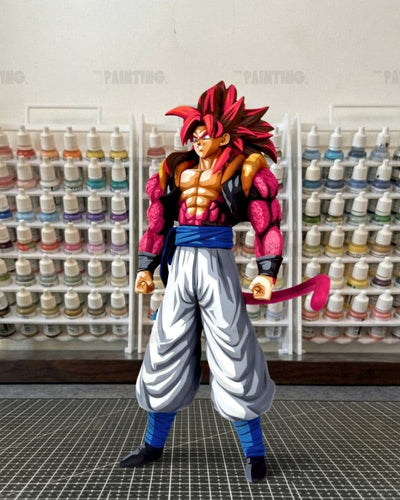 A detailed anime figurine of a Super Saiyan character with spiky red hair, muscular definition, and a pink tail, standing on a gray grid mat in front of shelves filled with paint bottles.