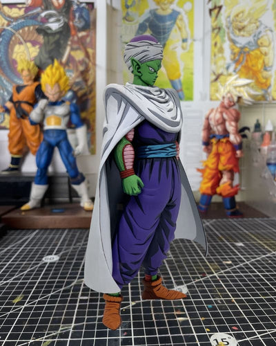 A detailed anime figurine of Piccolo Sempai from Dragon Ball Z, standing on a black gridded cutting mat with other collectible figures blurred in the background.