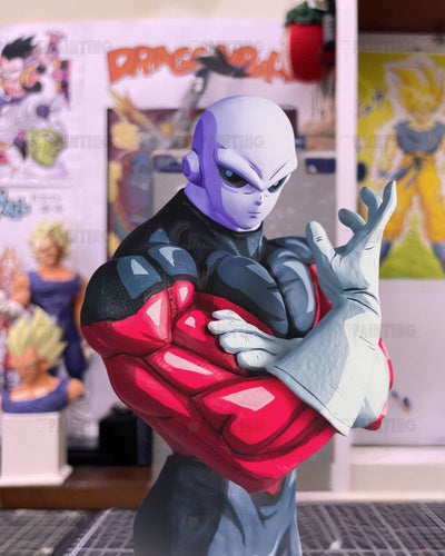 A Dragon Ball figure of the character Frieza with a purple head, black and red body armor, and white gloves, posed with arms crossed in front of a blurred room background with Dragon Ball posters.