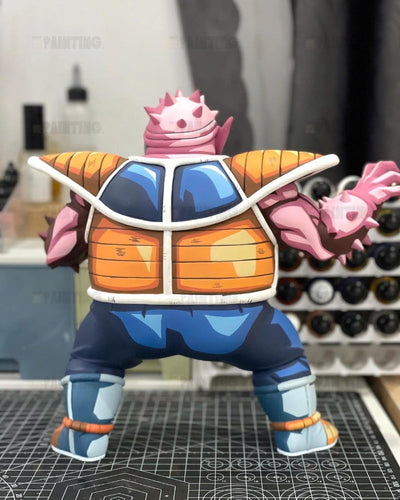 A colorful anime-style collectible figure shown from the back, featuring a pink spiky shell-like head, orange armor plating, blue body sections, and light blue boots, standing on a gridded work mat in a workshop setting.