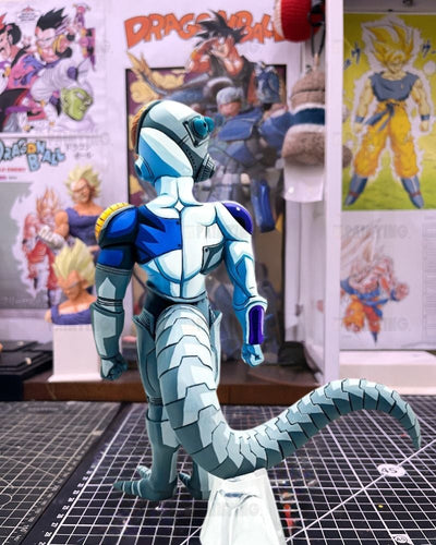 A detailed action figure or collectible character model shown from the back, featuring a blue and white armored design with a long segmented tail, standing on a cutting mat in front of a wall covered in Dragon Ball posters.