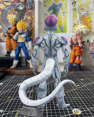 A detailed collectible figure of Frieza from Dragon Ball Z, shown from the back on a grid cutting mat with other anime figures in the background.