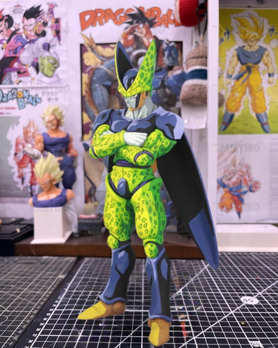 A Dragon Ball Z collectible figure of Cell, standing with arms crossed on a cutting mat, with Dragon Ball posters in the background.