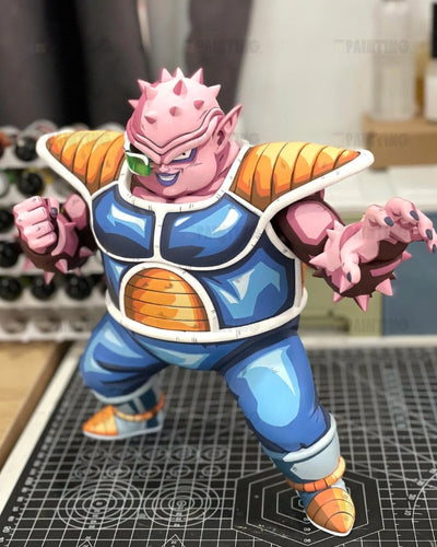 A collectible action figure of a pink-skinned Dragon Ball Z character in a blue and orange gi, posed dynamically on a black gridded cutting mat with a blurred workshop background.