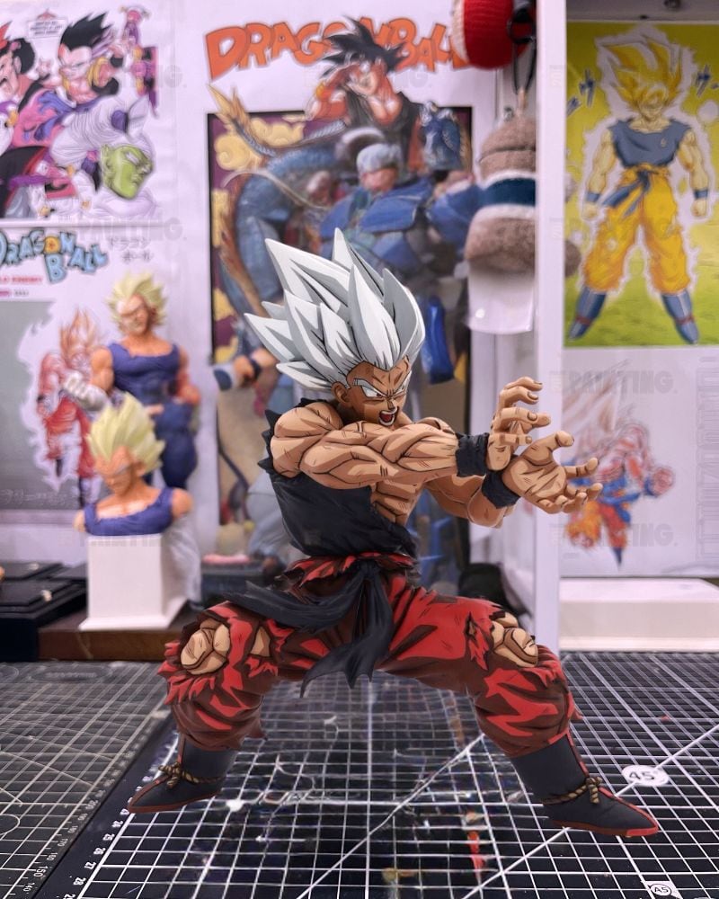A detailed collectible action figure of a Super Saiyan character from Dragon Ball, posed dynamically on a black gridded cutting mat with anime posters in the background.