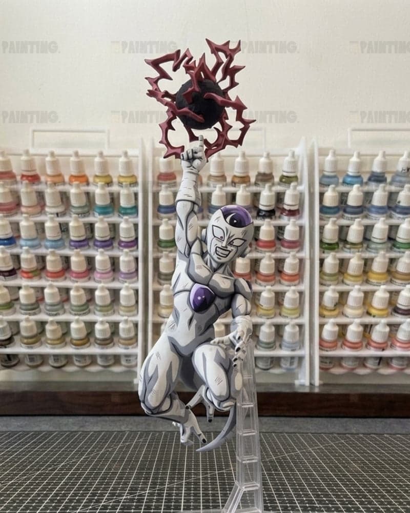 A painted anime figurine of a white and purple female character climbing a clear ladder while holding a red spiky object, set against a background of shelves filled with paint bottles.
