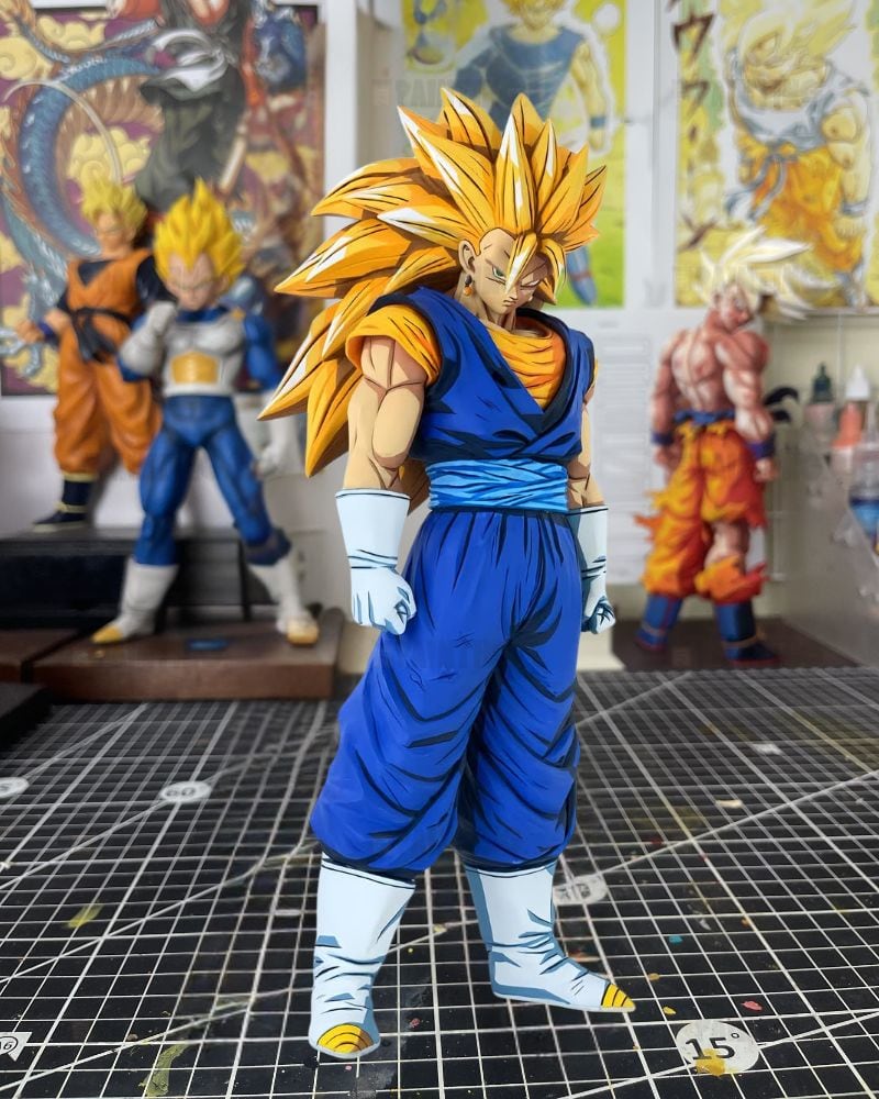 A detailed collectible figurine of a Super Saiyan Gohan from Dragon Ball Z, standing on a gridded cutting mat in a hobby room with other anime statues in the background.