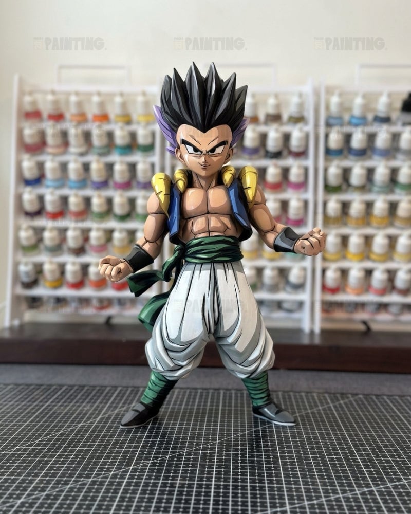 A detailed anime action figure of Gogeta from Dragon Ball Z, standing on a black gridded cutting mat with shelves of miniature figures blurred in the background.