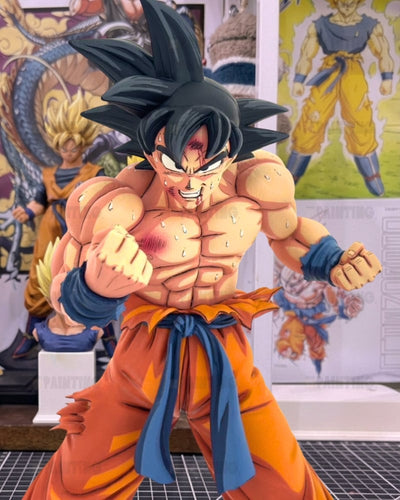 A detailed collectible figure of Goku from Dragon Ball Z in a fighting pose, featuring muscular definition, spiky black hair, an orange gi with a blue sash, and battle scars, set against a background of Dragon Ball posters and other figures.