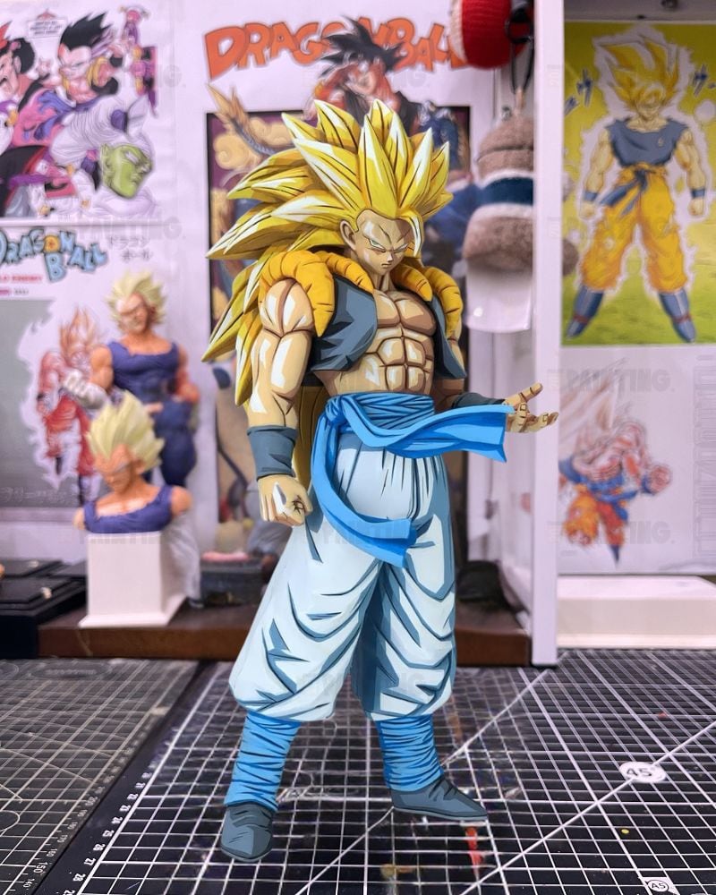 A detailed anime figurine of a Super Saiyan character in a fighting pose, standing on a gridded cutting mat with Dragon Ball posters and displays in the background.