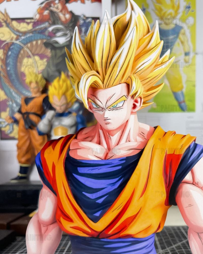 A stylized anime character bust resembling Super Saiyan Gohan from Dragon Ball, with spiky blond hair, an orange and blue outfit, and a blurred room background featuring posters and figurines.