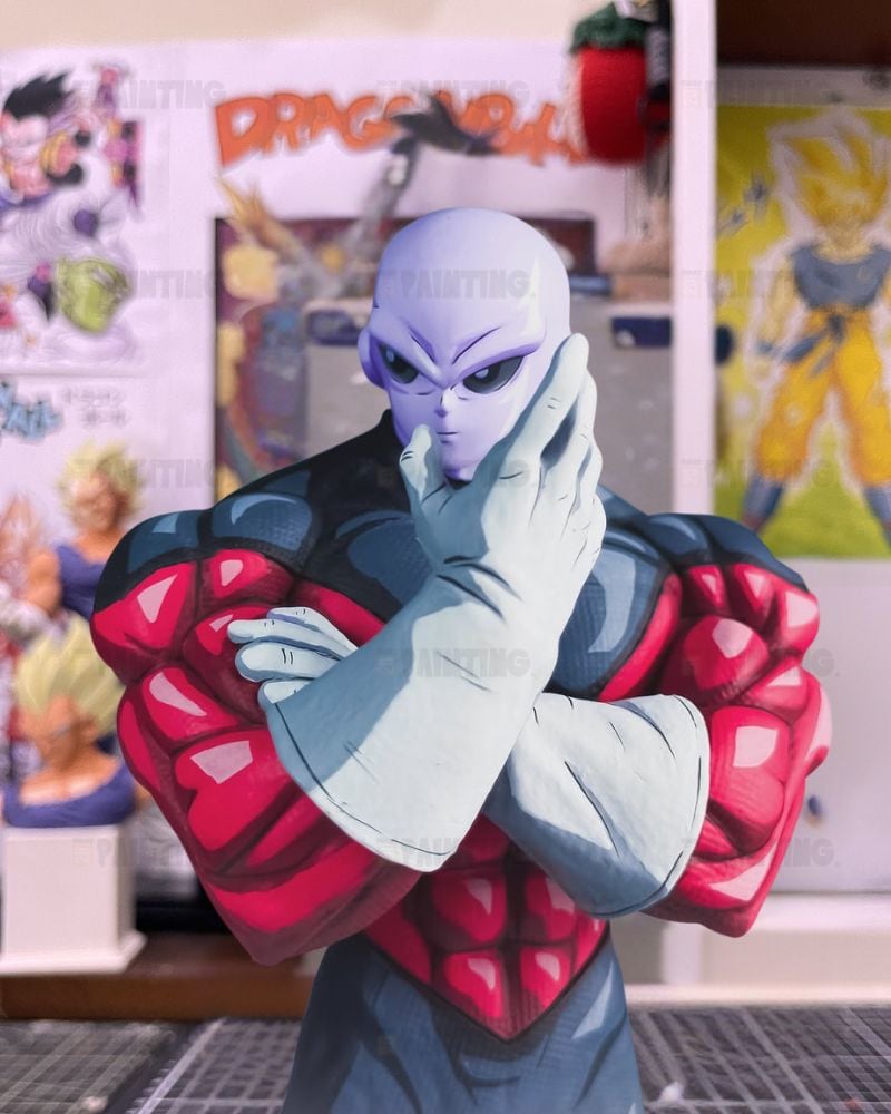 A Dragon Ball Z collectible figure of the character Panthro, featuring his signature red and black armored chest, pale lavender skin, and white gloves, posed with arms crossed in front of a themed background of Dragon Ball posters.