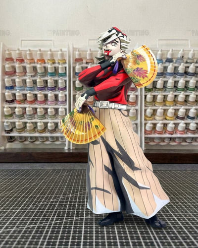 A collectible anime figure of Zenitsu Agatsuma from Demon Slayer, styled in a miniature craft room with shelves of paint bottles in the background.