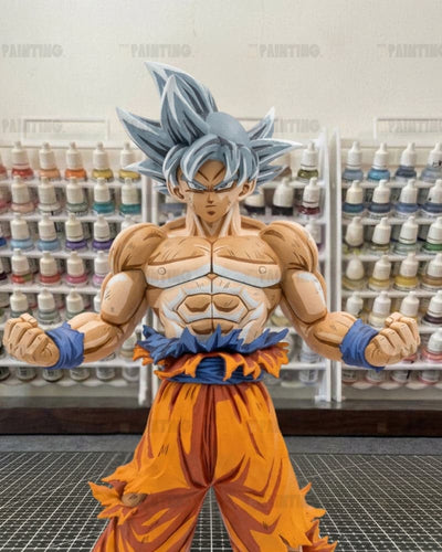 A painted anime figurine of Goku in his Super Saiyan form, standing in a workshop with shelves of paint bottles in the background.