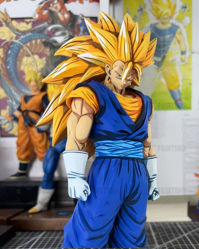 A detailed collectible figure of Goku in his Super Saiyan form from Dragon Ball, wearing his classic blue and orange gi with white gloves, standing in a room with anime posters in the background.