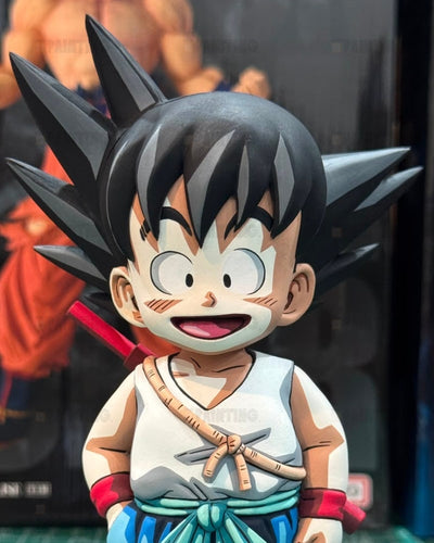 A close-up of a stylized anime figurine resembling Goku from Dragon Ball, with spiky black hair, a white sleeveless top, blue pants, and red wristbands, shown against a dark blurred background.