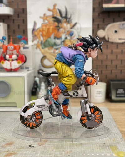 A detailed collectible figurine of a character riding a small white and gray bicycle with orange accents, displayed on a clear stand in a room setting.