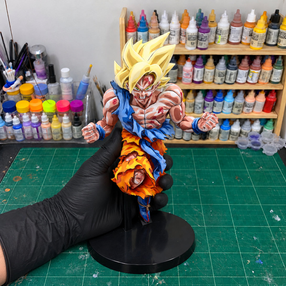 Super Saiyan Son Goku Jump 50th Anniversary Figure Repaint — held securely in one gloved hand in the workshop